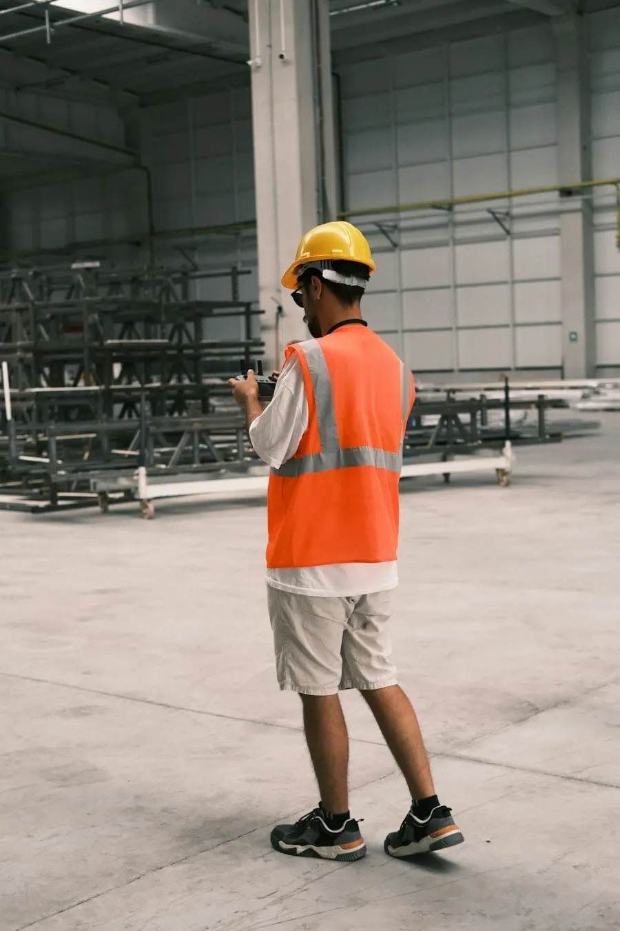 A technician in a hard hat and safety vest checking a tablet in a warehouse